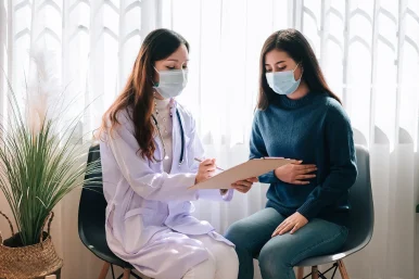 asian-doctor-visit-examines-young-adult-woman-hospital-with-stomach-ache-doctor-checking-up-consulting-health-care-wearing-mask-protect-covid19-pandemic 2